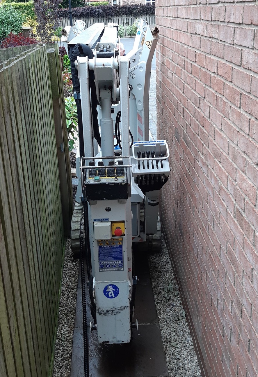 Scarlett Grace, High Reaching Solutions 13m tracked spiderlift cherrypickers squeezing between fence and wall to gain access to rear of house for building maintenance near Malton, York, North Yorkshire.