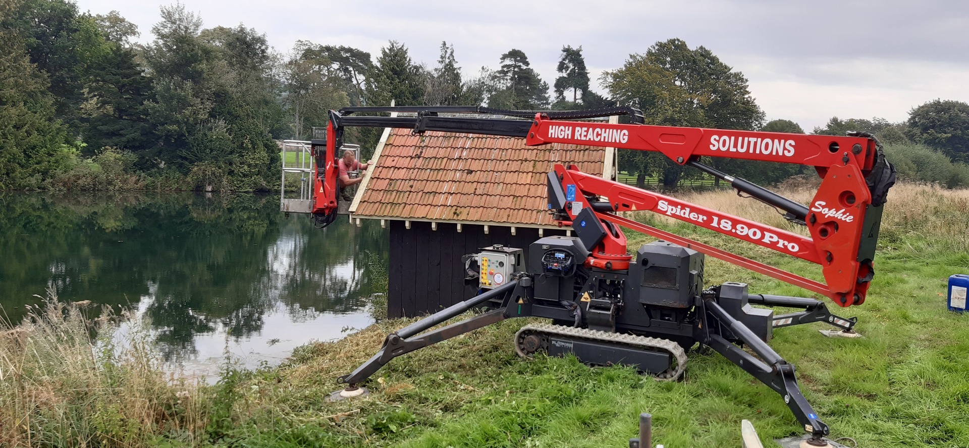 Another view of Sophie, High Reaching Solutions 18m tracked spiderlift cherrypicker, booming out over a lake assisting a decorator with building maintenance of a Boat House near Malton, North Yorkshire.