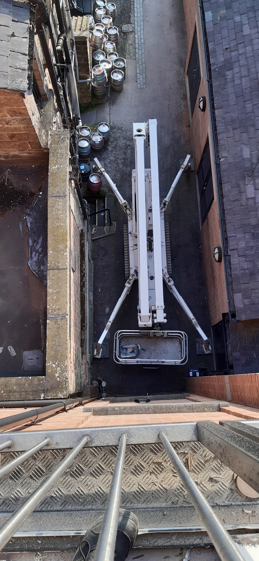 Selina, High Reaching Solutions 22m Lithium hybrid tracked spiderlift cherrypicker viewed from above, sited in a tight alleyway with her legs placed in the narrow setting, assisting with window repairs on a 5-story property in Harrogate, North Yorkshire.